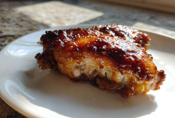 Close-up of a juicy, glazed Chipotle Honey Chicken Thighs piece on a white plate.