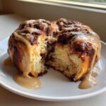 A single, fluffy Cookie Butter Cinnamon Roll pulled apart, showing the soft interior and drizzled with thick cookie butter glaze.