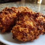 Two pieces of golden brown, extra crispy Copycat Country Chicken resting on a white plate.