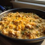 Close-up of a skillet filled with creamy Cajun chicken rice topped with melted cheddar cheese and green peppers.