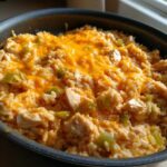 A skillet filled with creamy Cajun chicken rice, featuring chunks of chicken, green peppers, and topped with melted orange cheddar cheese.