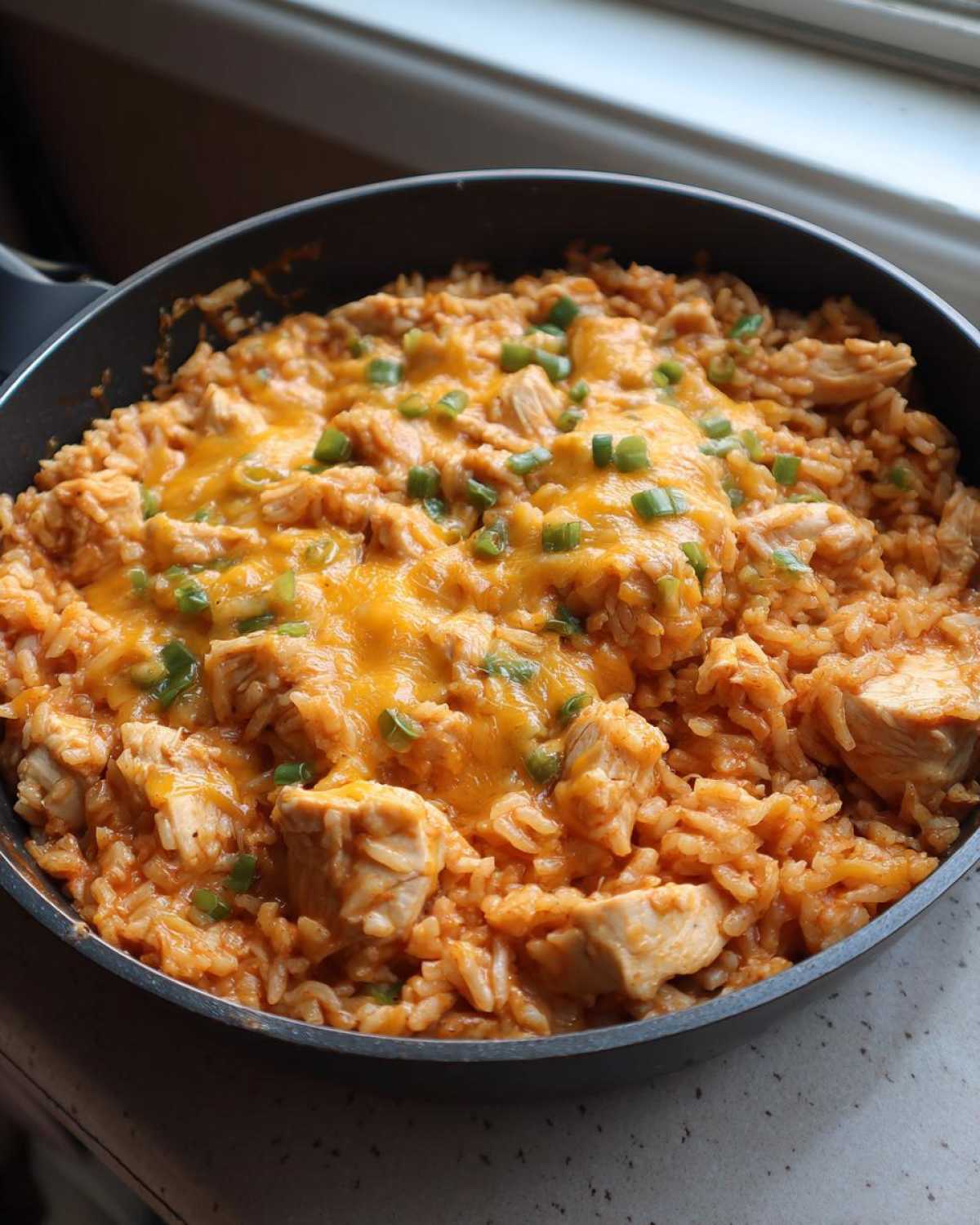 A close-up view of Creamy Cajun Chicken Rice cooked in a black skillet, topped with melted cheddar cheese and sliced green onions.