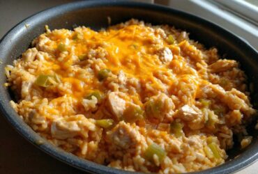 A skillet filled with creamy Cajun chicken rice, featuring chunks of chicken, green peppers, and topped with melted orange cheddar cheese.