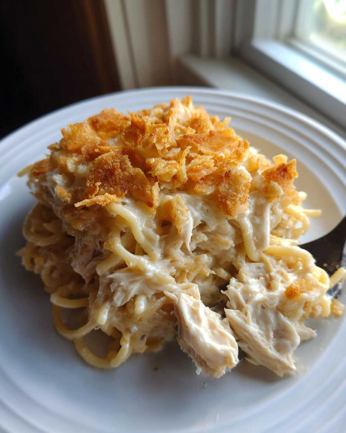 A close-up serving of creamy Chicken Spaghetti topped with golden, crispy fried onions or breadcrumbs on a white plate.