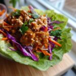 A single serving of Crunchy Thai Chicken Wraps featuring saucy chicken, shredded carrots, and purple cabbage in a crisp lettuce cup.