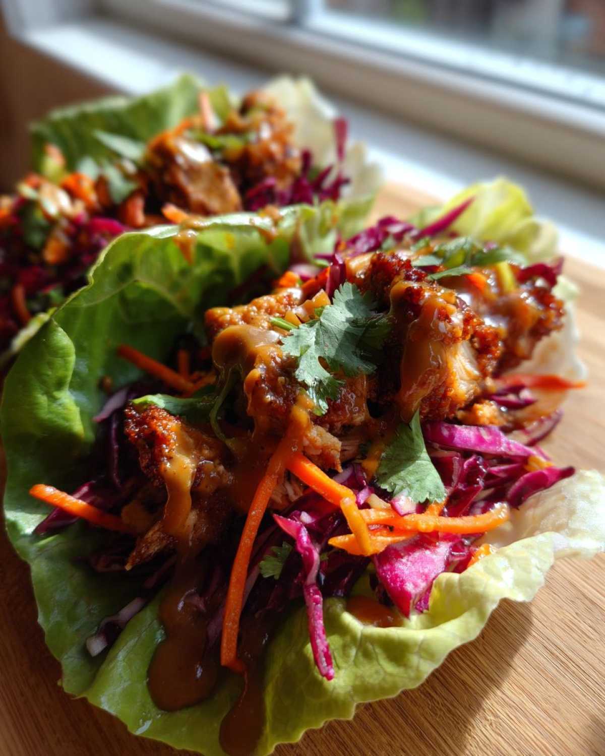 Two close-up servings of Crunchy Thai Chicken Wraps featuring crispy chicken, shredded cabbage, carrots, and peanut sauce in lettuce cups.