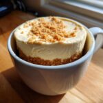 A finished Decadent Cheesecake Mug Recipe, featuring a creamy cheesecake filling and graham cracker crust in a white mug.