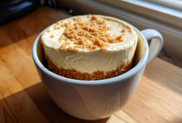 A finished Decadent Cheesecake Mug Recipe, featuring a creamy cheesecake filling and graham cracker crust in a white mug.