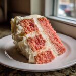 A moist slice of Decadent Hawaiian Guava Cake featuring pink layers and thick white frosting, served on a white plate.