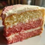 Close-up of a slice of Decadent Hawaiian Guava Cake showing alternating yellow and pink layers with white frosting.