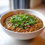 A close-up of a white bowl filled with rich Easy Green Lentil Dal, topped generously with fresh chopped cilantro.
