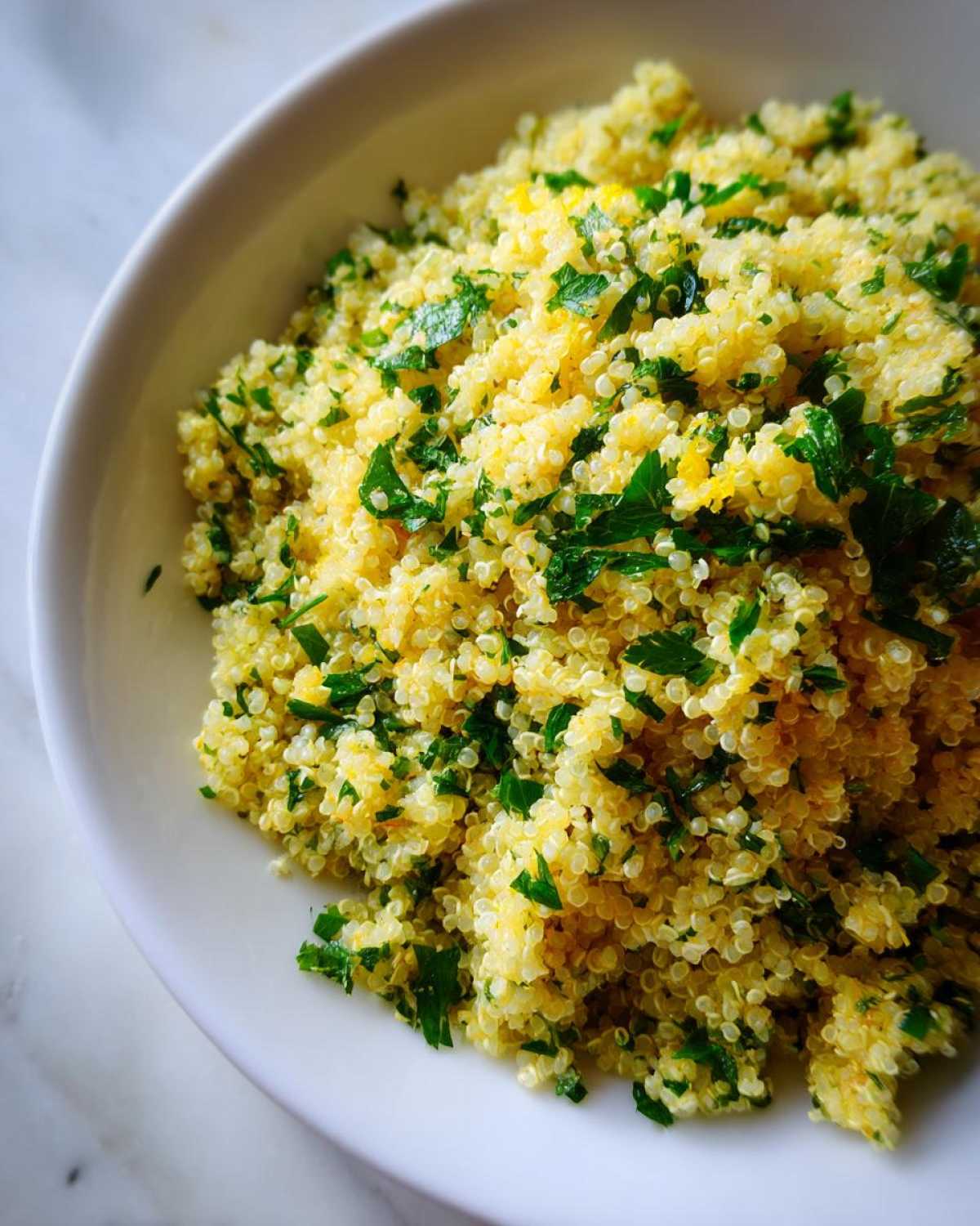 Close-up of fluffy Easy Lemon Herb Quinoa mixed with bright green chopped parsley in a white bowl.