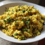 A close-up of fluffy, yellow Easy Lemon Herb Quinoa garnished with fresh chopped parsley in a white bowl.