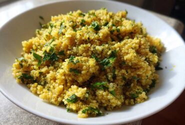 A close-up of fluffy, yellow Easy Lemon Herb Quinoa garnished with fresh chopped parsley in a white bowl.