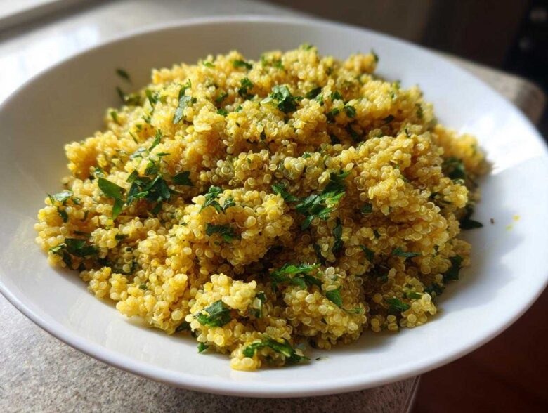 A close-up of fluffy, yellow Easy Lemon Herb Quinoa garnished with fresh chopped parsley in a white bowl.