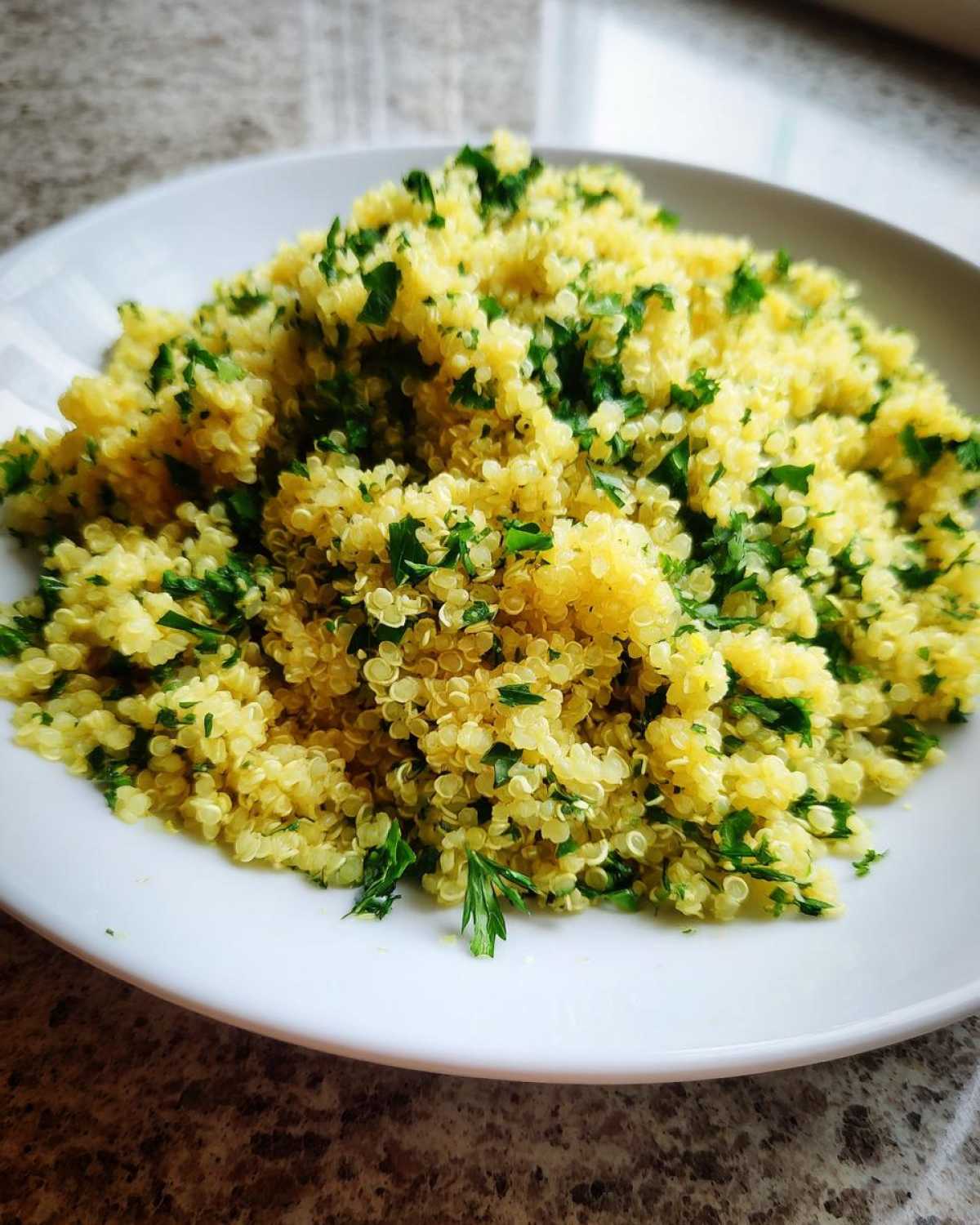 Close-up of fluffy, yellow Easy Lemon Herb Quinoa generously topped with fresh chopped parsley on a white plate.