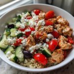 Close-up of an Easy Mediterranean Chicken Bowl featuring seasoned chicken, quinoa, cucumber, tomatoes, olives, and feta cheese.