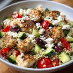A close-up of an Easy Mediterranean Chicken Bowl featuring seasoned chicken pieces, quinoa, cucumbers, tomatoes, olives, and feta cheese.