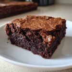 Close-up of a rich, dark square brownie showing a dense, fudgy texture and shiny top crust, illustrating the solution for Brownies Missing That Fudgy Texture.