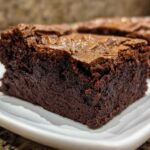 Close-up of a rich, dark, fudgy brownie slice showing its dense interior and shiny top crust.