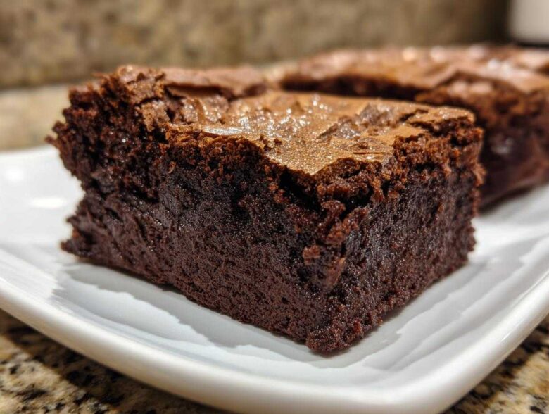 Close-up of a rich, dark, fudgy brownie slice showing its dense interior and shiny top crust.