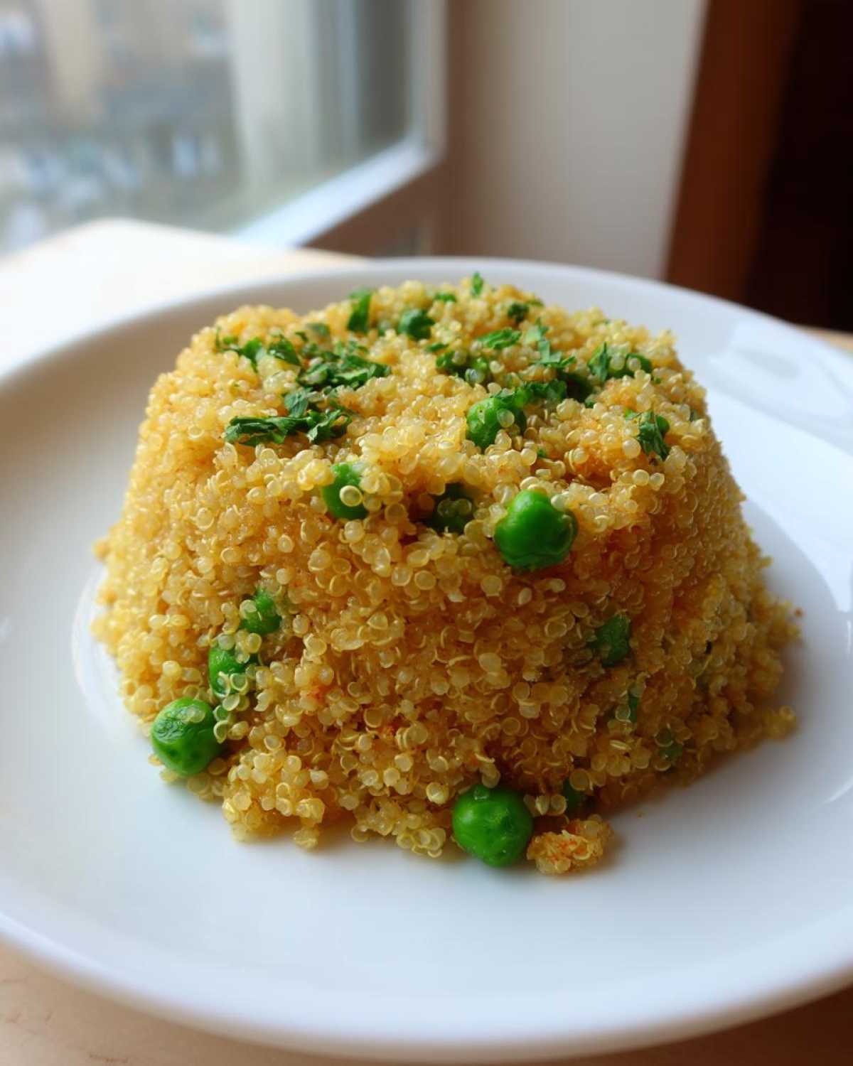 A molded serving of Garlic Butter Quinoa Green Peas garnished with fresh parsley on a white plate.