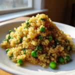 A mound of fluffy Garlic Butter Quinoa Green Peas served on a white plate, brightly lit by natural light.
