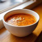 A close-up of rich, orange Garlic Tikka Masala Sauce garnished with herbs in a white bowl.