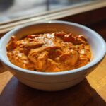 A close-up of creamy, orange Garlic Tikka Masala Sauce with visible spices served in a white bowl.