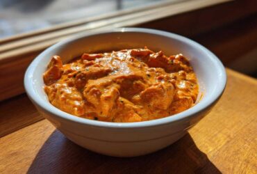 A close-up of creamy, orange Garlic Tikka Masala Sauce with visible spices served in a white bowl.
