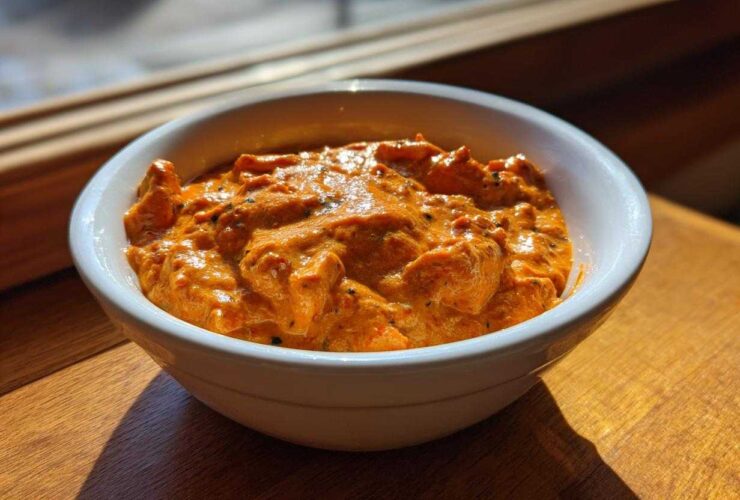 A close-up of creamy, orange Garlic Tikka Masala Sauce with visible spices served in a white bowl.