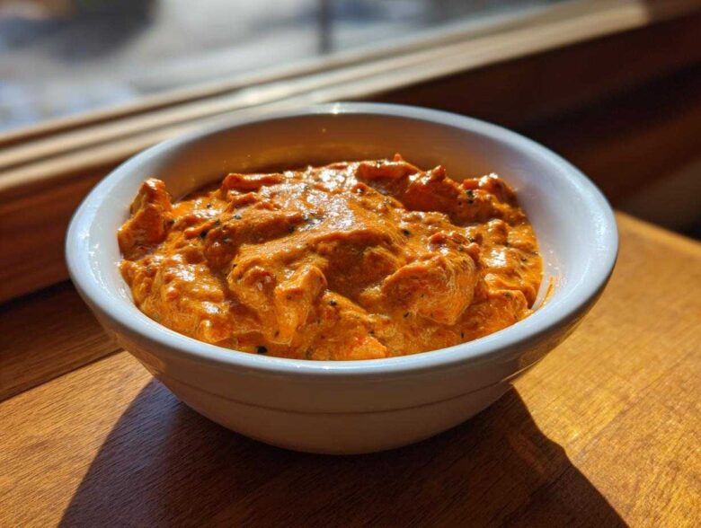 A close-up of creamy, orange Garlic Tikka Masala Sauce with visible spices served in a white bowl.