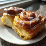 Two gooey, glazed Pistachio Cream Cinnamon Rolls sitting on a small white plate bathed in sunlight.