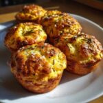 Close-up of several golden brown Focaccia Muffins topped with flaky sea salt and fresh rosemary sprigs.