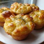 A close-up of several golden brown Focaccia Muffins, glistening with oil and topped with coarse sea salt and fresh rosemary sprigs.