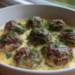 Seven browned Greek meatballs submerged in a creamy, yellow lemon sauce and generously topped with fresh dill.