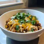 Close-up of a white bowl filled with Ground Turkey Rice Bowls, topped with melted cheddar cheese and fresh cilantro.