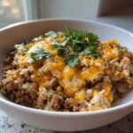A close-up view of a white bowl filled with Ground Turkey Rice Bowls, topped with melted cheddar cheese and fresh cilantro.
