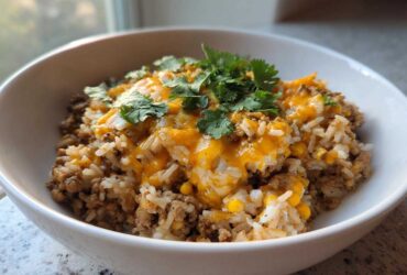 A close-up view of a white bowl filled with Ground Turkey Rice Bowls, topped with melted cheddar cheese and fresh cilantro.
