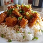 Close-up of sticky, glazed chicken pieces served over fluffy white coconut rice, garnished with green onions, representing Hawaiian Chicken Coconut Rice.