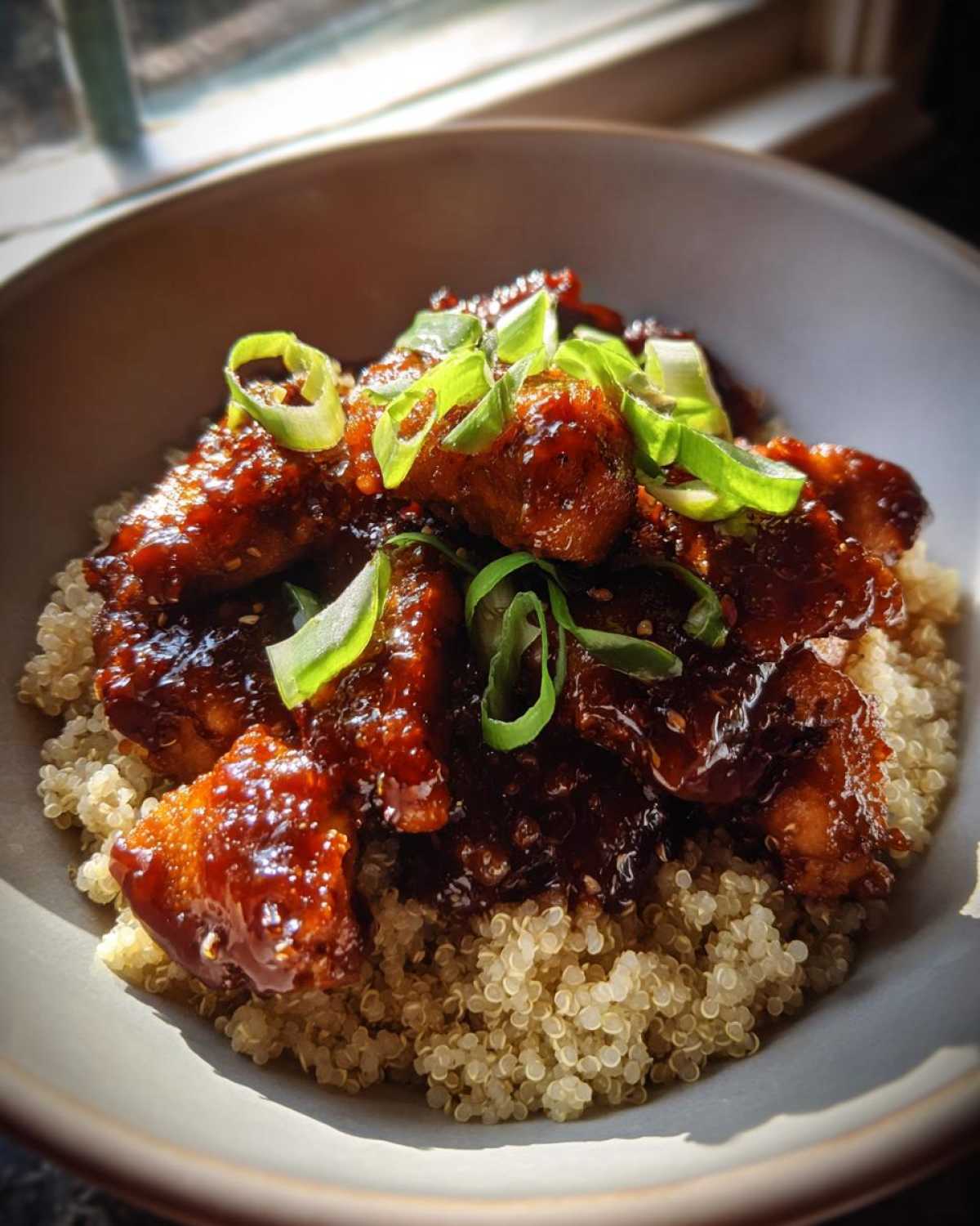 Close-up of Honey Garlic Chicken Quinoa, featuring glazed chicken pieces over a bed of fluffy quinoa, topped with sliced green onions.