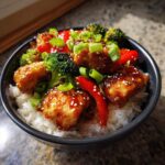 Close-up of a Honey Lime Chicken Rice Bowl featuring glazed chicken pieces, broccoli, red peppers, and scallions over white rice.