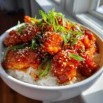 Close-up of Honey Sriracha Chicken Rice Bowls, featuring glazed chicken pieces over white rice, topped with sesame seeds and green onions.