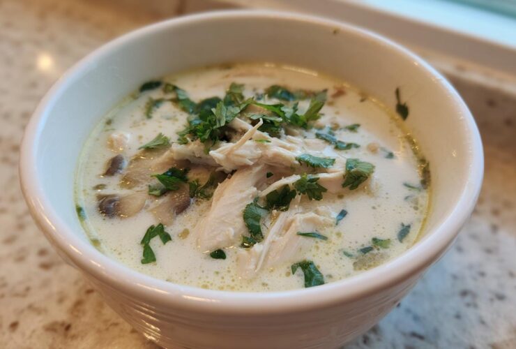 Close-up of a white bowl filled with Irresistible Thai Chicken Soup, featuring shredded chicken, mushrooms, and fresh cilantro garnish.