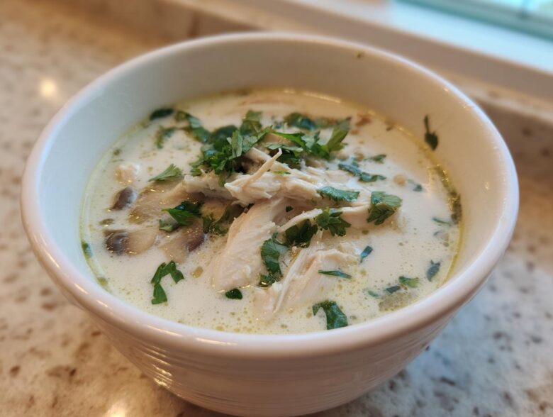 Close-up of a white bowl filled with Irresistible Thai Chicken Soup, featuring shredded chicken, mushrooms, and fresh cilantro garnish.