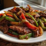 A close-up of a serving of Keto Beef Pepper Steak featuring glossy, saucy beef strips mixed with vibrant green and red bell peppers and onions.