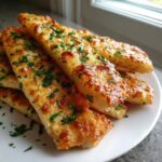 Close-up of cheesy, golden Keto Garlic Breadsticks topped with fresh chopped parsley on a white plate.