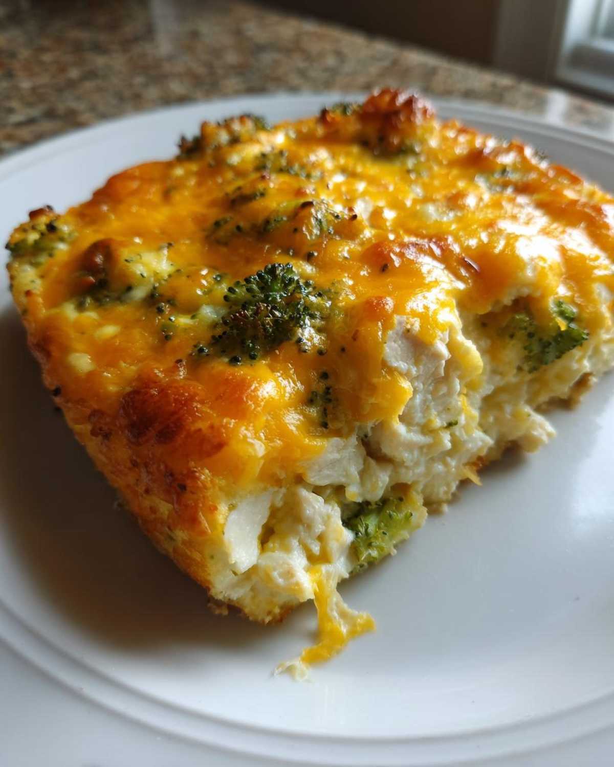 A close-up of a square serving of Low Carb Chicken Casserole topped with melted cheddar cheese and visible broccoli florets.