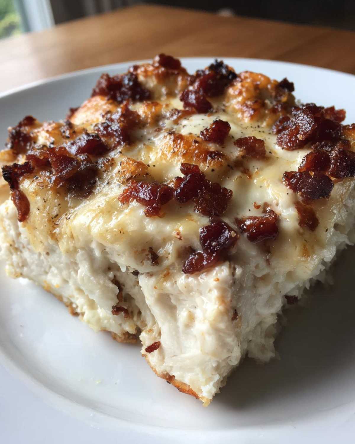 A close-up of a square serving of Malibu Chicken Cheesy Bacon Chicken with melted cheese and crispy bacon bits on top.