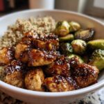 Close-up of a Maple Dijon Chicken Bowl featuring glazed chicken pieces, quinoa, and roasted Brussels sprouts in a white bowl.